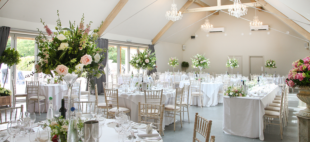 The Orchard Barn at Blackwell Grange is set up for an elegant wedding reception with tall pink and ivory floral table centrepieces